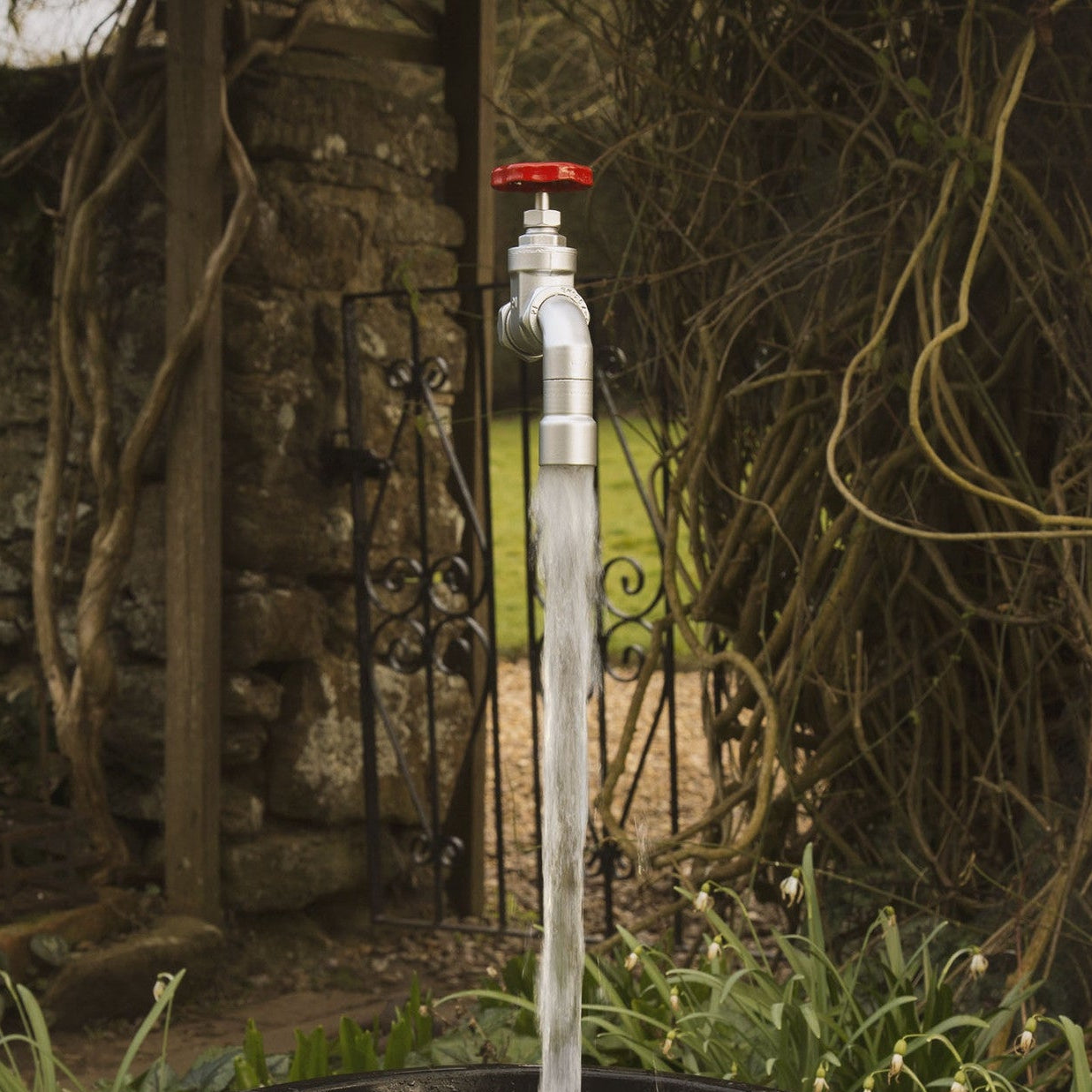 A floating tap water feature with a red gate valve tap  with water flowing magically set in a garden environment.