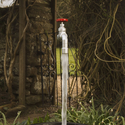 A floating tap water feature with a red gate valve tap  with water flowing magically set in a garden environment.