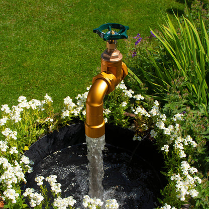 A half oak barrel water feature with a large brass tap installed in the center, surrounded by plants and set in an outdoor setting.