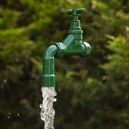 A floating tap water feature with a solid brass tap and soldered copper spout, running water, set in a garden environment with flowers in the background.