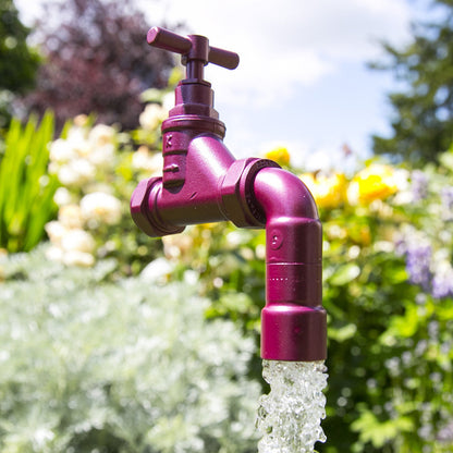 A floating tap water feature with a solid brass tap and soldered copper spout, running water, set in a garden environment with flowers in the background.