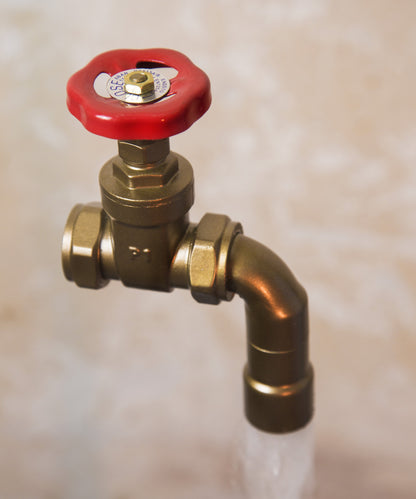A floating tap water feature with a red gate valve tap with water flowing into the magically set in a industrial business environment.
