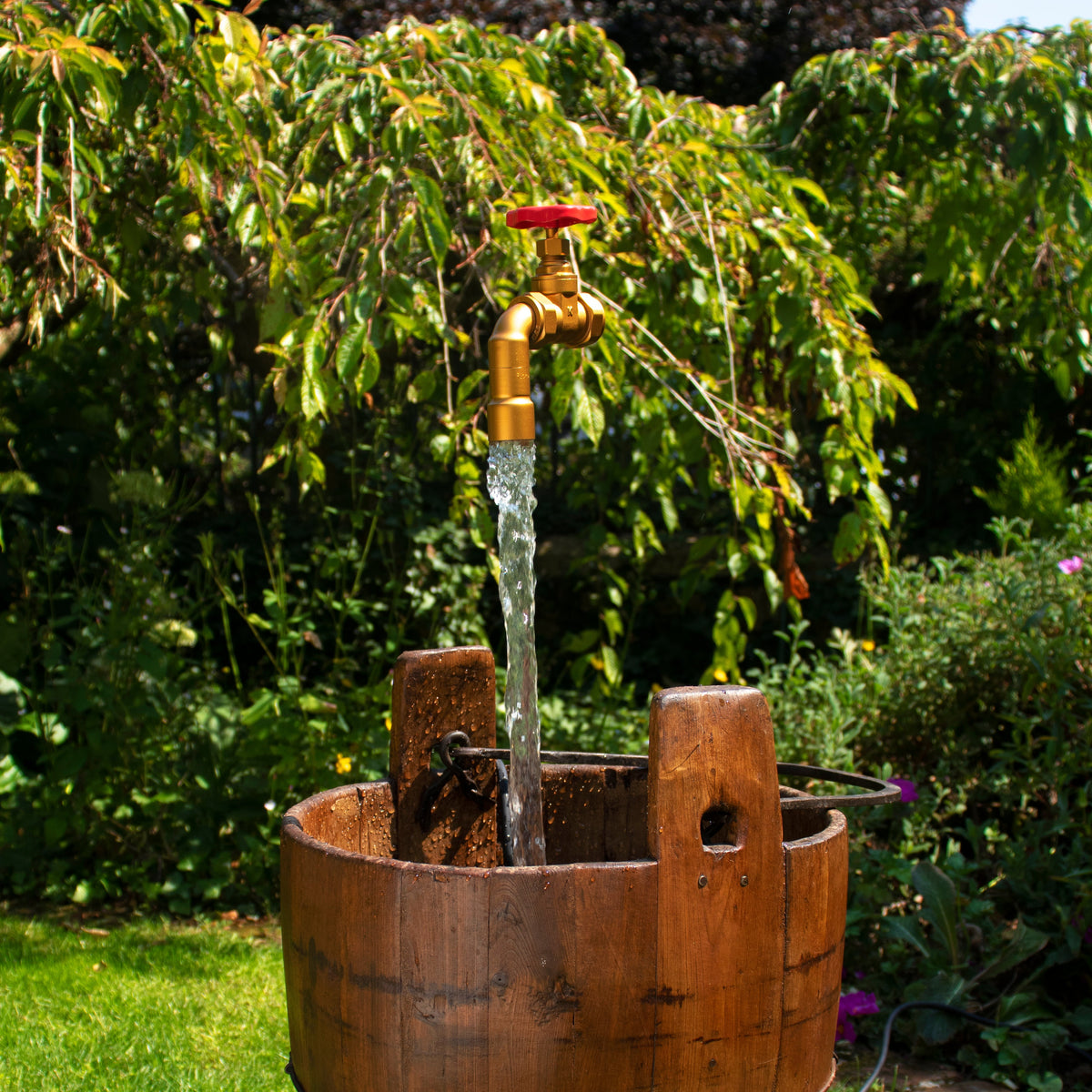 Vintage pail with a golden floating tap suspended in the middle set in a green and floral garden setting