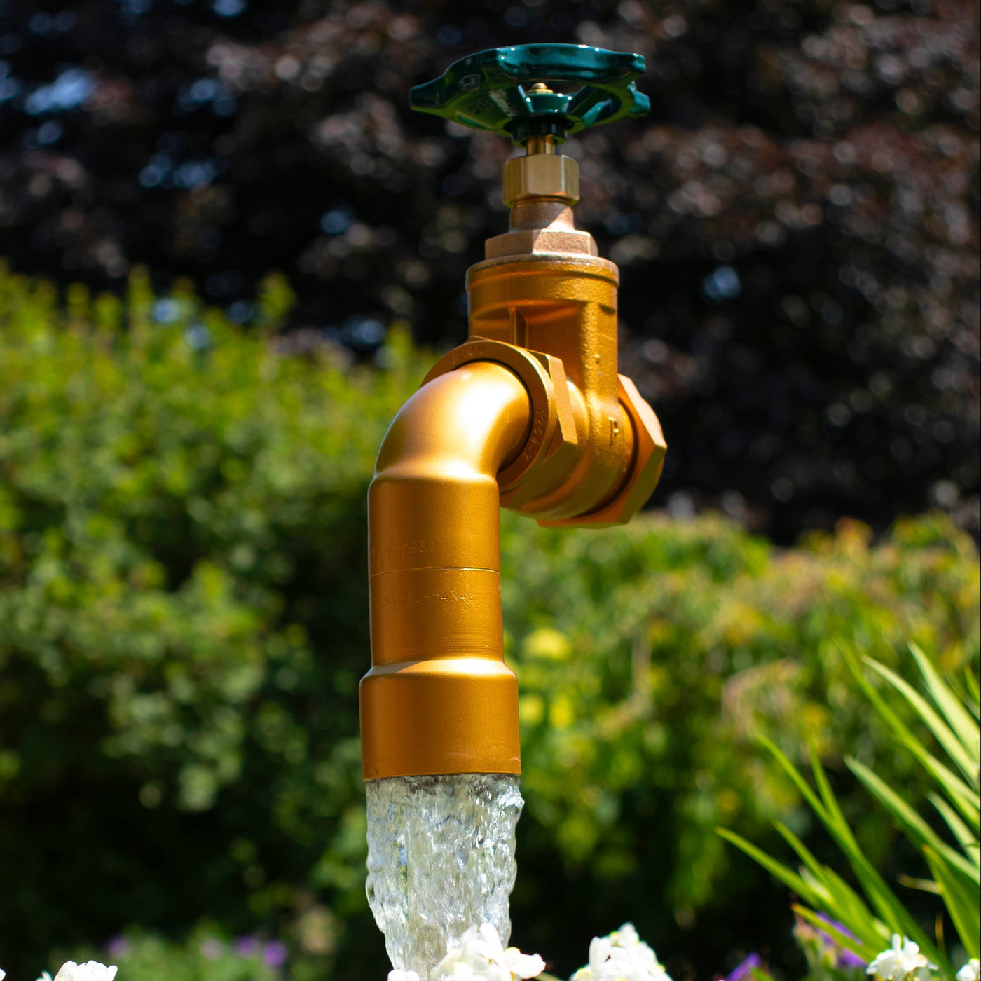 A half oak barrel water feature with a large brass tap installed in the center, surrounded by plants and set in an outdoor setting.