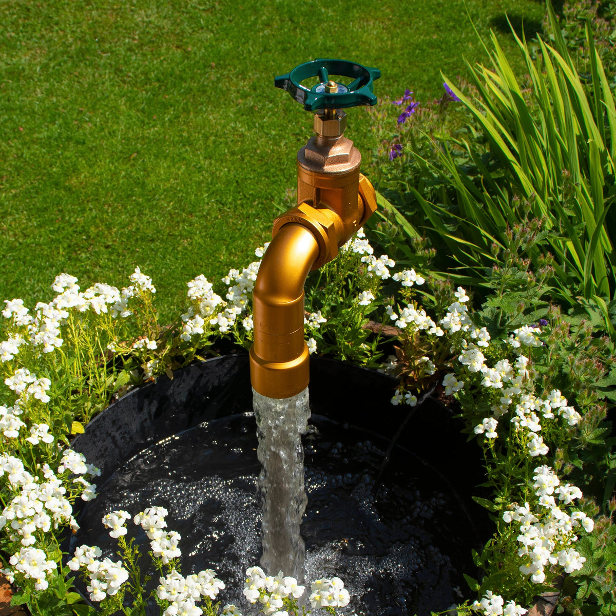 A large floating tap installed on top of a barrel surrounded by plants, with a clear sky and trees in the background.