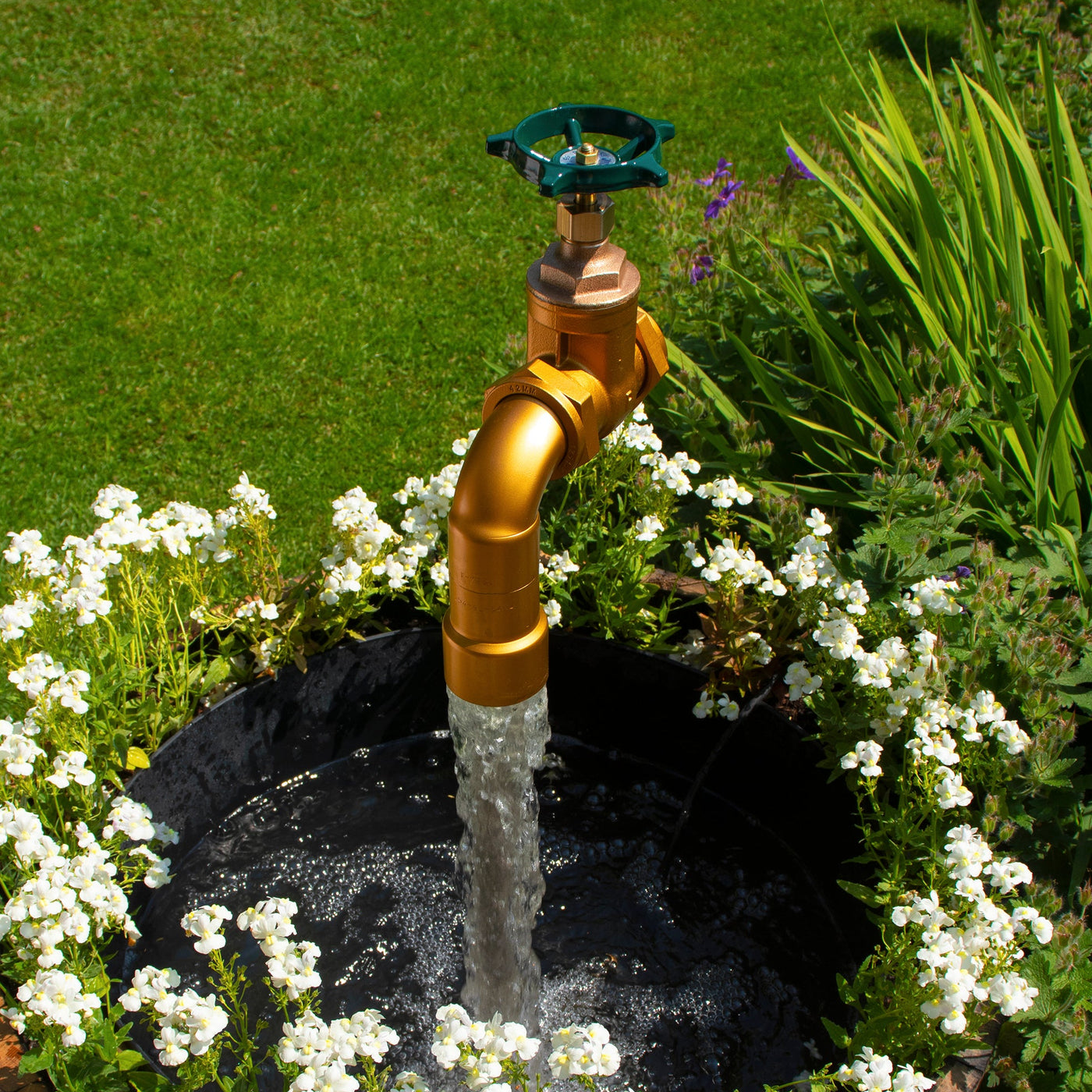 A large floating tap installed on top of a barrel surrounded by plants, with a clear sky and trees in the background.