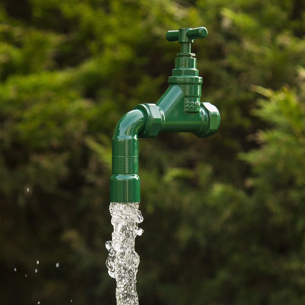 A green floating tap sits suspended magically on real flowing water with a green garden background 