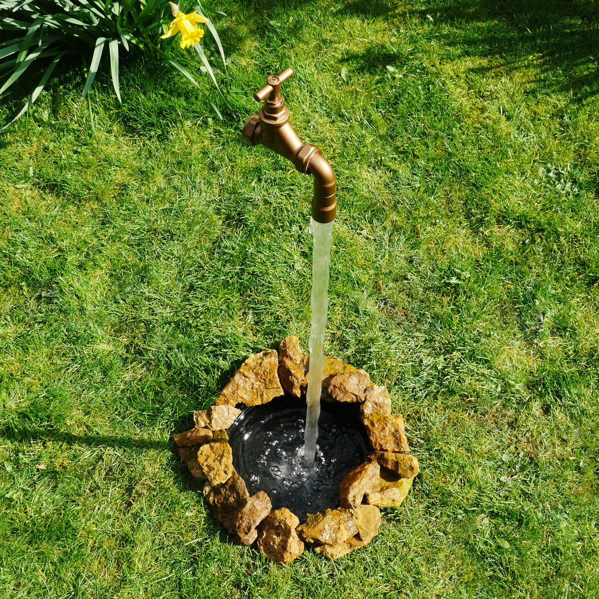 Magical fountain with a bronze faucet on a grassy area