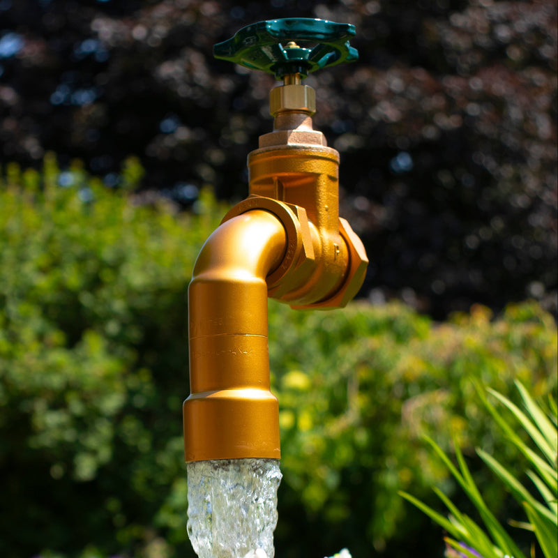 A large floating tap installed on top of a barrel surrounded by plants, with a clear sky and trees in the background.
